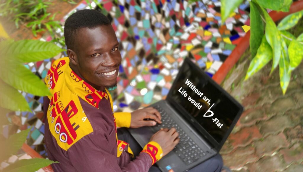 Founder Adiko sitting while holding a laptop computer. He is smiling towards the camera. On the laptop screen, it is written, "without art, life would b-flat."